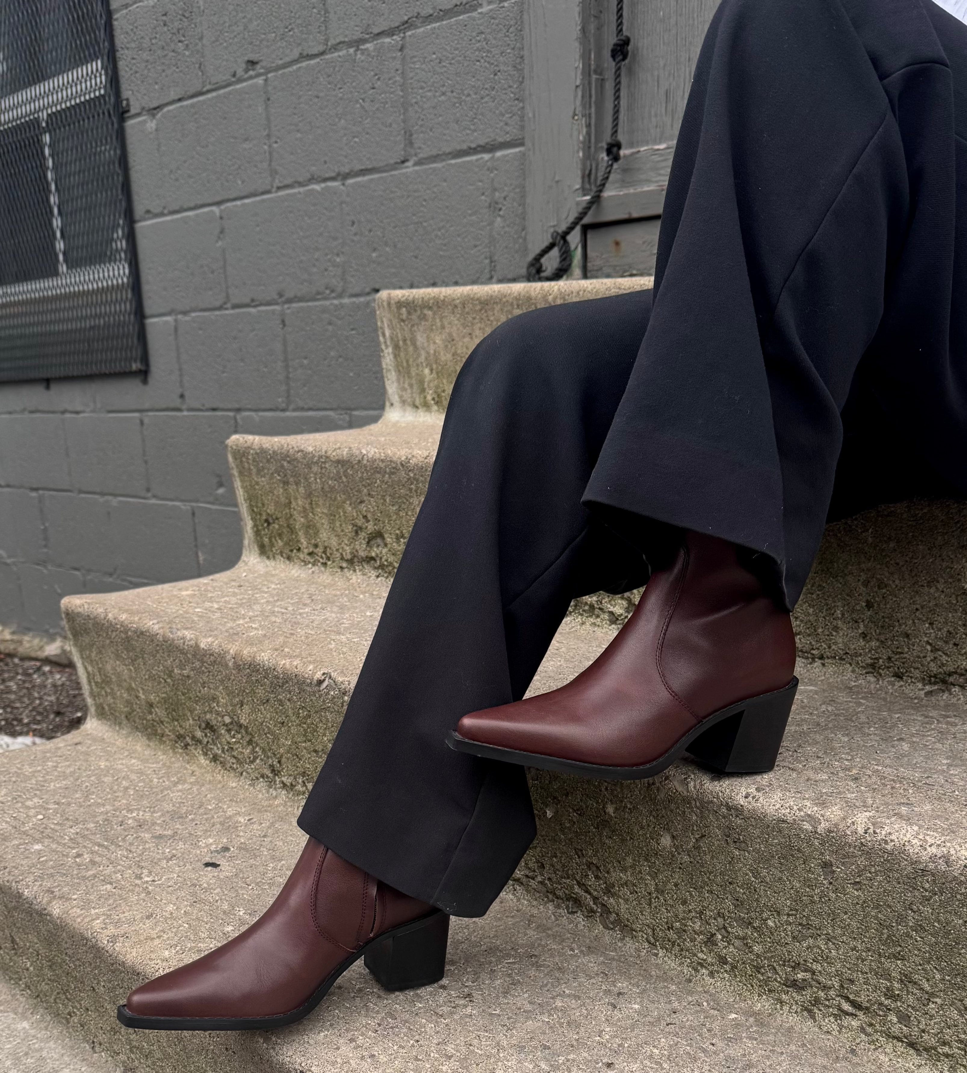 Person wearing dark pants and brown shoes sitting on concrete steps.