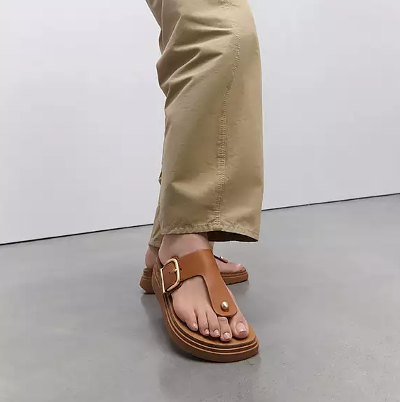 Light brown leather toe-post sandal with gold buckle. 